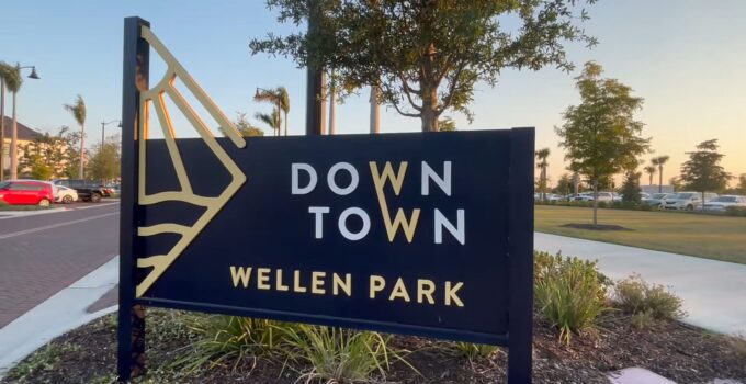 Signage for Downtown Wellen Park set in a landscaped area with palm trees and parked cars in the background