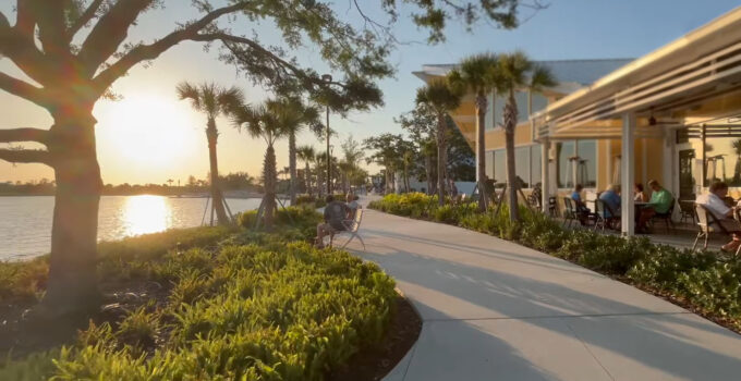 Scenic view of a waterfront walkway at Wellen Park lined with palm trees and lush greenery at sunset.