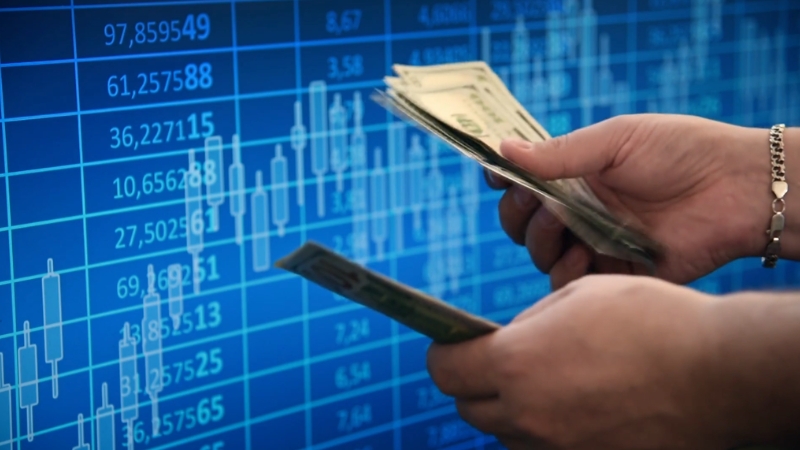 Hands holding cash in front of financial charts representing profit, cost, and revenue measurement